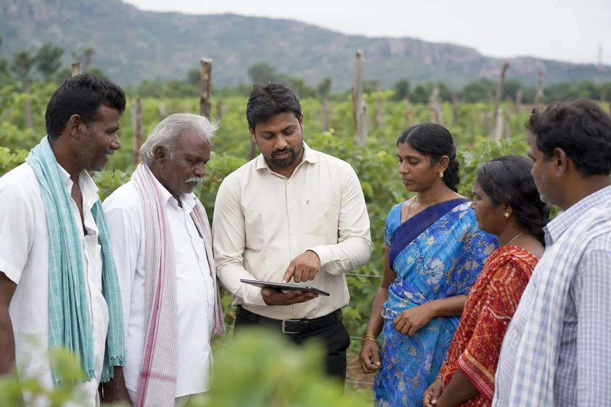 Farmers and a field coordinator reviewing information on a tablet