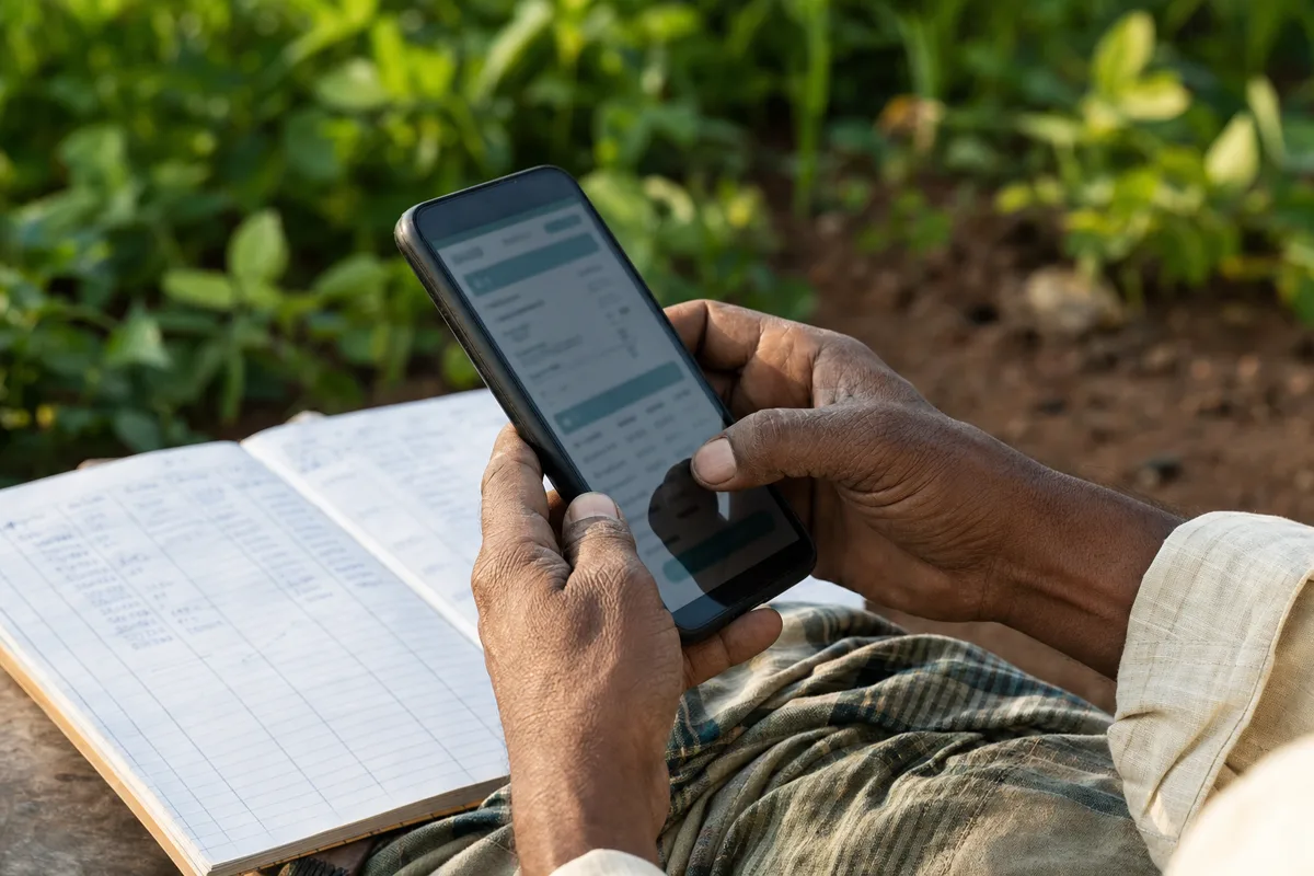 Farmer using a phone beside a farm record book in a field